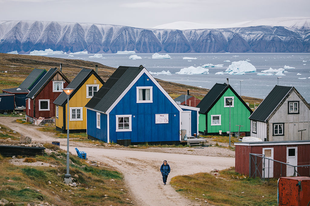 Adventure Canada - Colourful houses, blue, yellow and green with icebergs in background