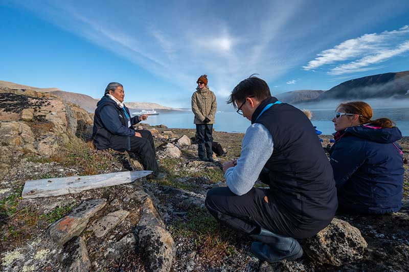 Adventure Canada - People sitting beside water on rocky ground