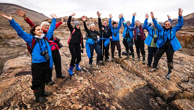 Adventure Canada - People standing on edge of cliff with arms raised