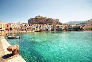 Sicily in background with people swimming in clear water - Just You Travel